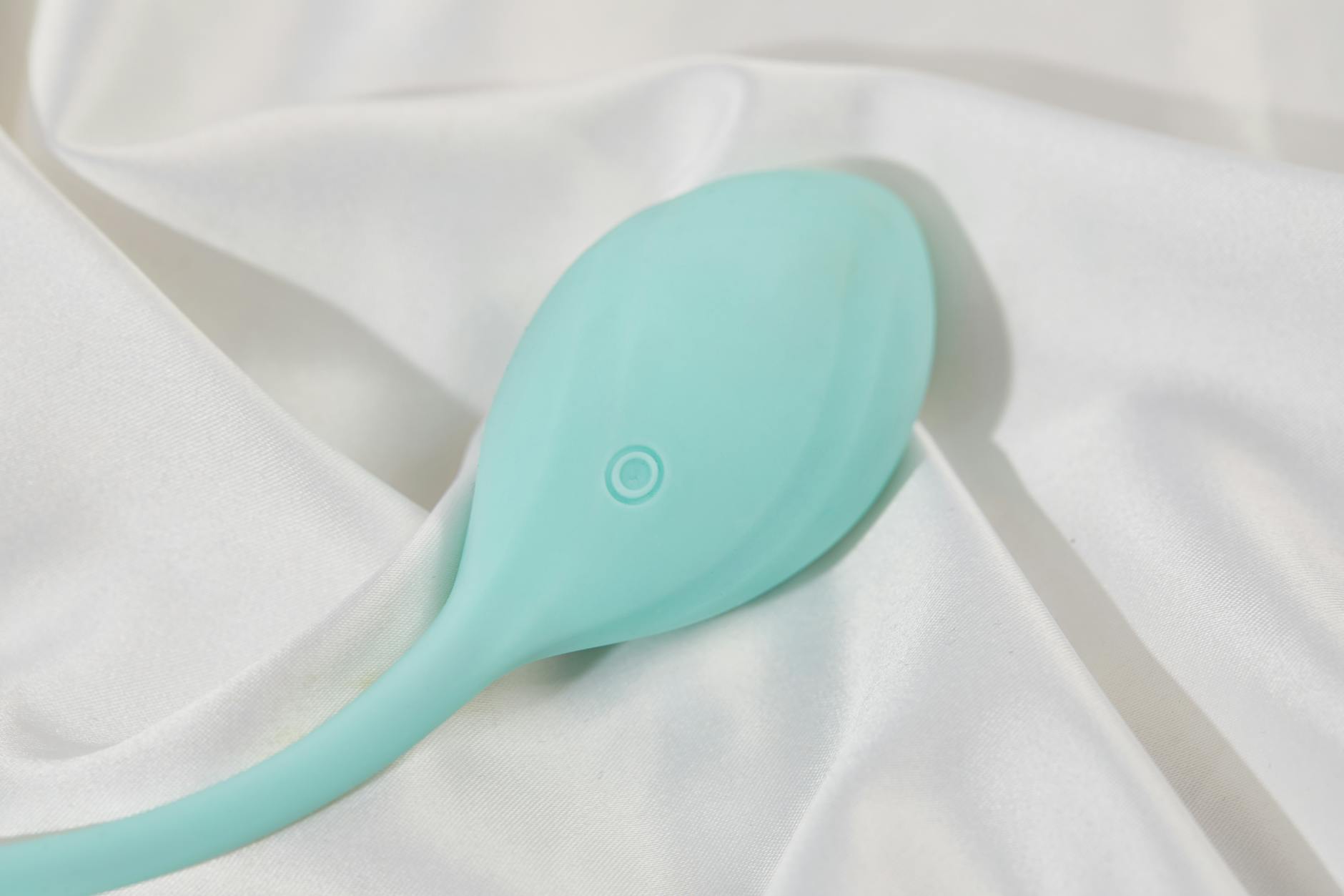 Ein stilvoller tealblauen Vibrator auf glatter weißer Seidenstoff, perfekt für Lifestyle-Bilder im Erwachsenenbereich.