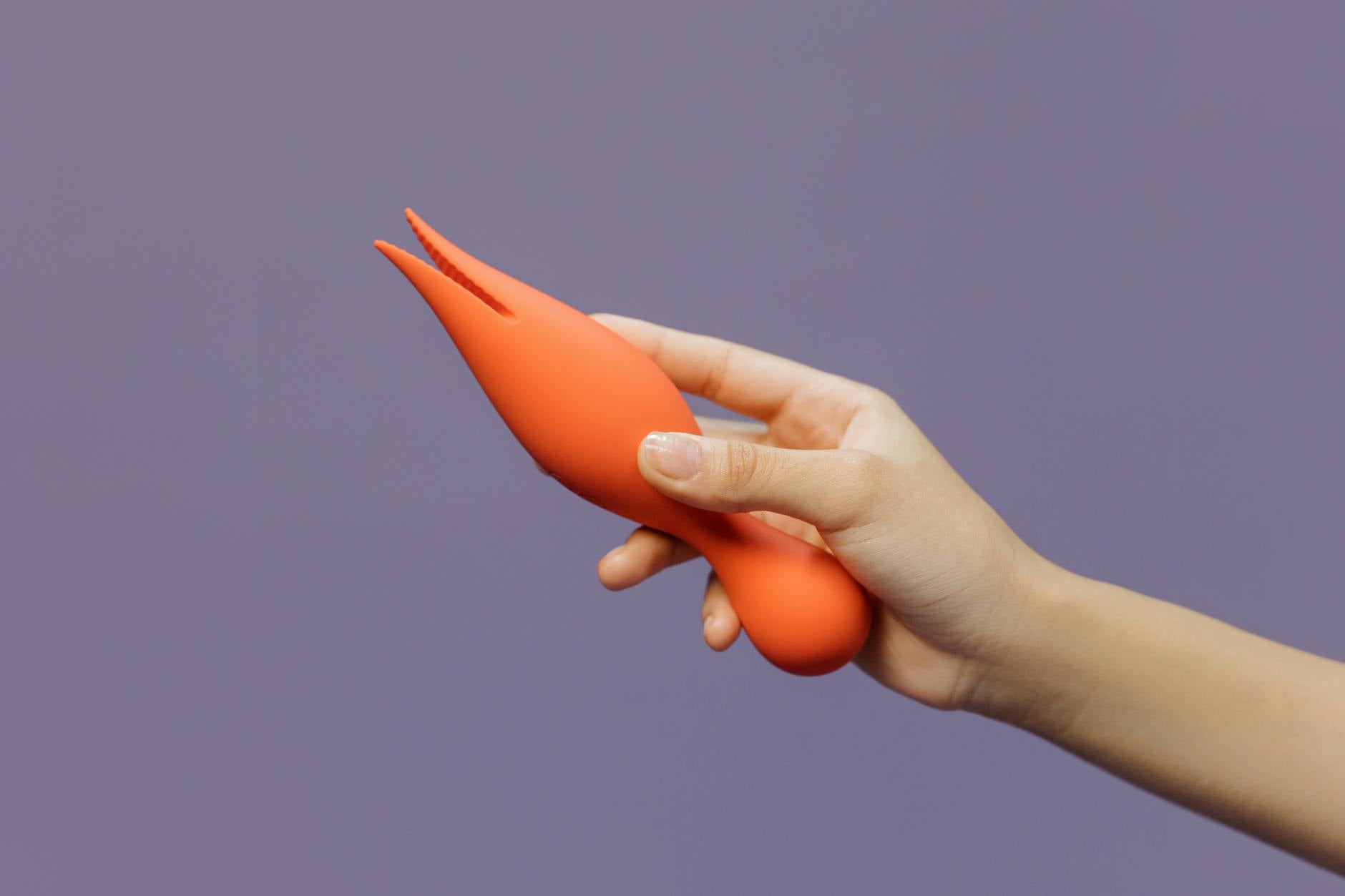 Close-up of a hand holding a lemon vibrator against a minimalistic purple backdrop, showcasing sensuality and pleasure.