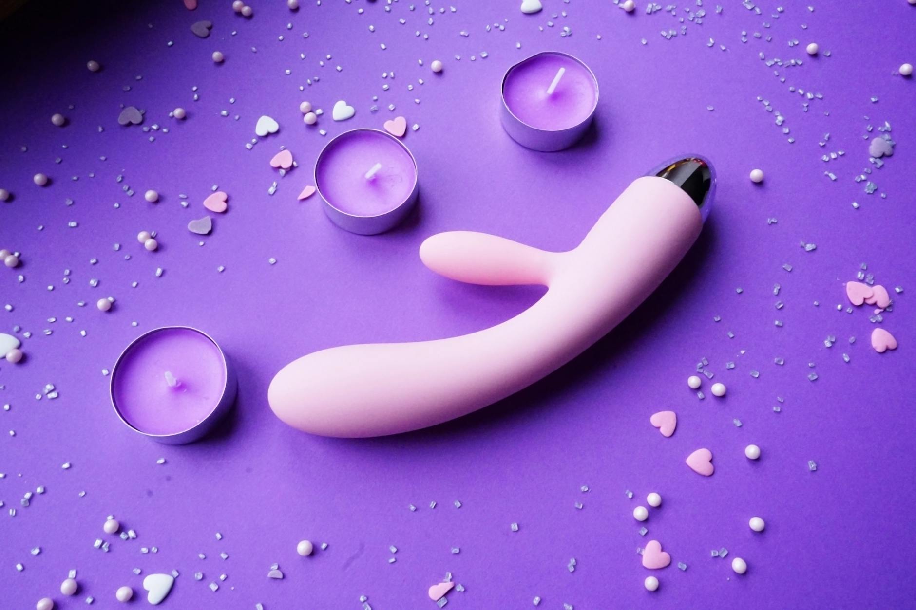 Pink lemon vibrator on purple background with heart confetti and candles for romantic recovery